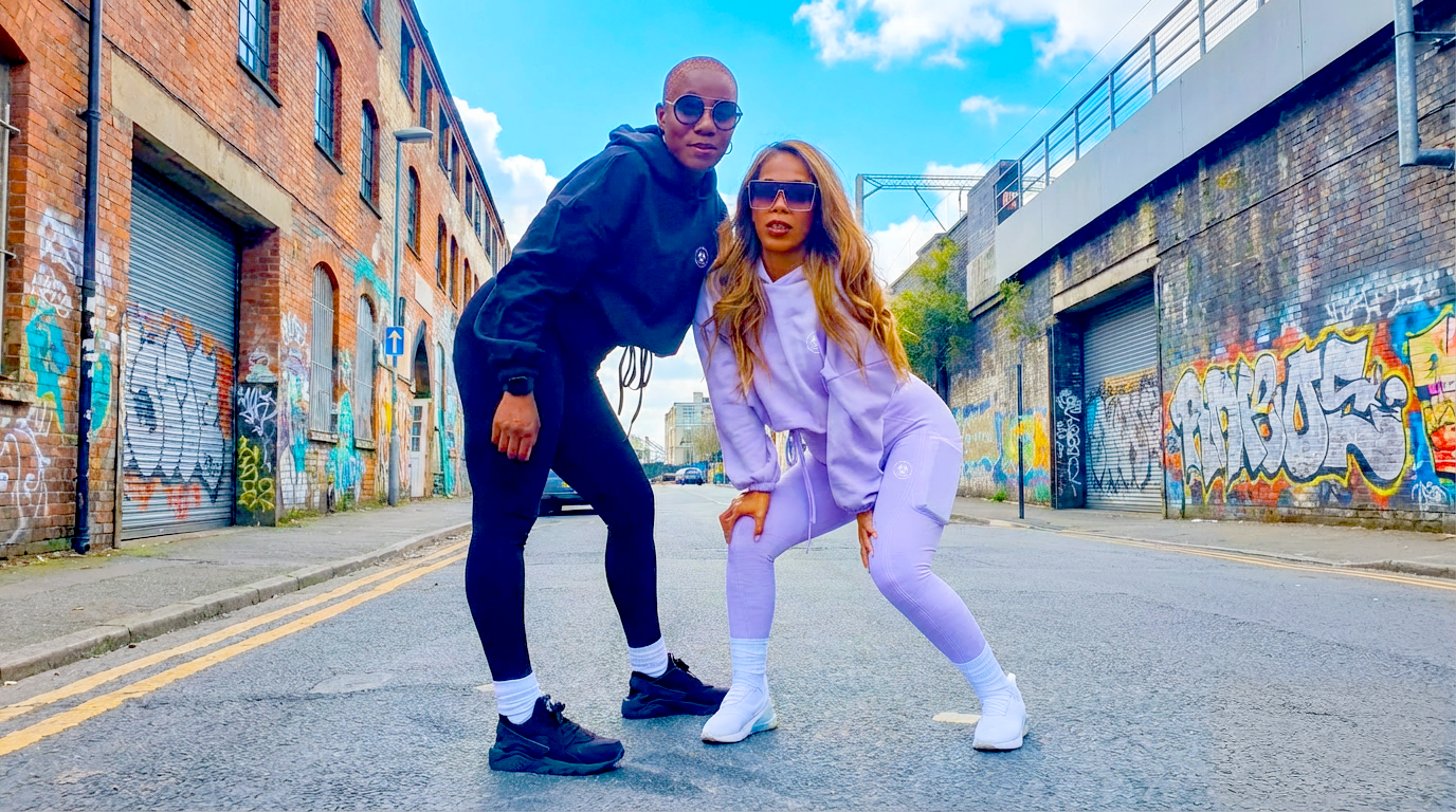 Two people posing in S.P Branded Clothing on a street with graffiti-covered walls.